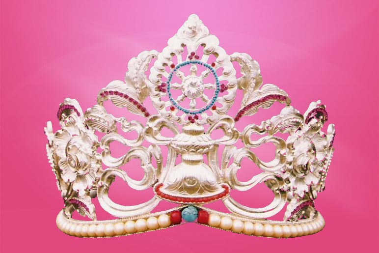 The Miss Tibet crown, in intricate silver filigree of Tibetan symbols,
            with outlines of red coral and pearls, a turqoise stone in the center,
            on a deep pink background